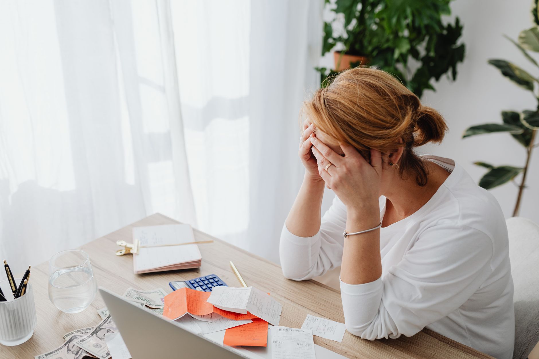 Femme stressée par des reçus financiers à un bureau, gérant des dépenses et des calculs.