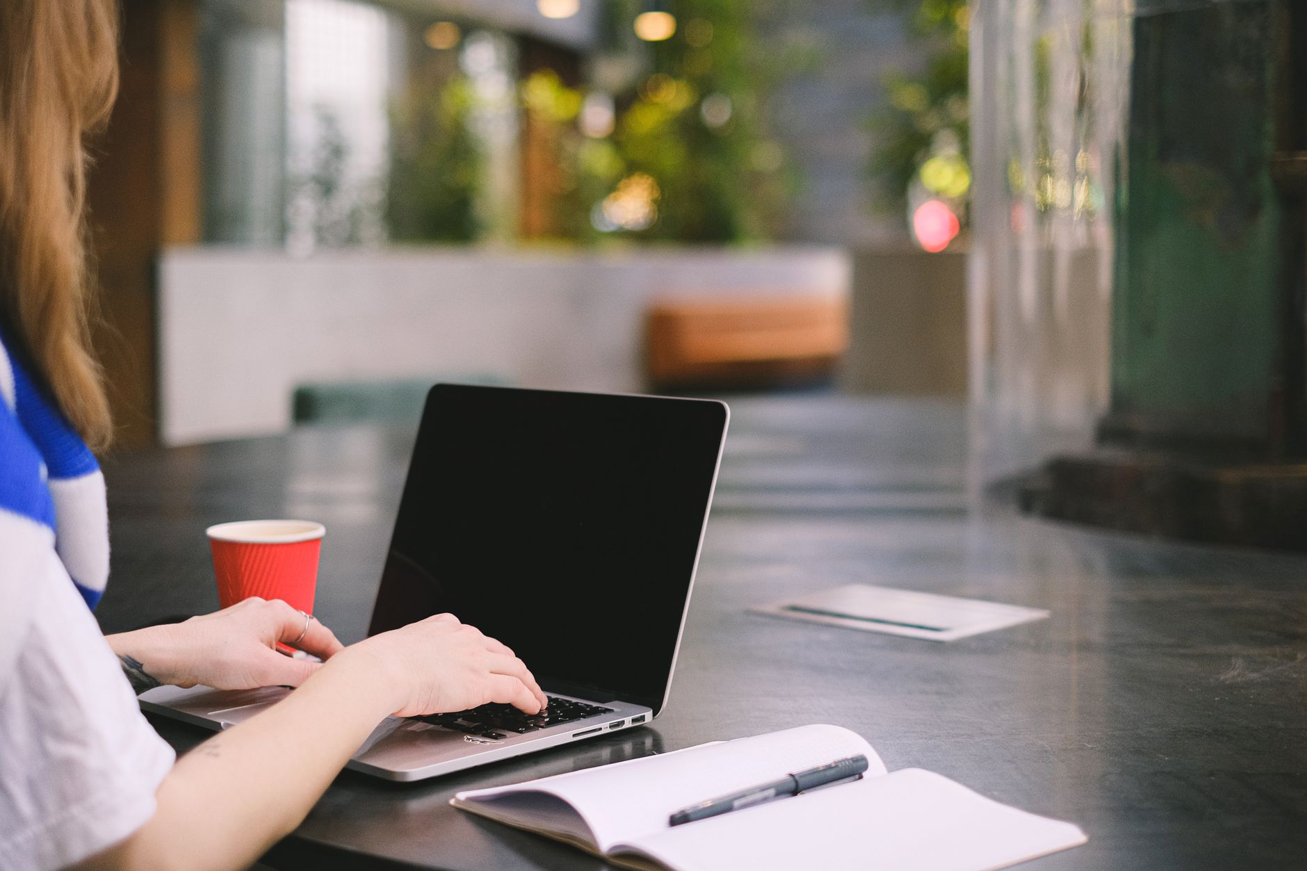 Personne tapant sur un ordinateur portable dans un espace de travail intérieur moderne avec du café et un carnet.