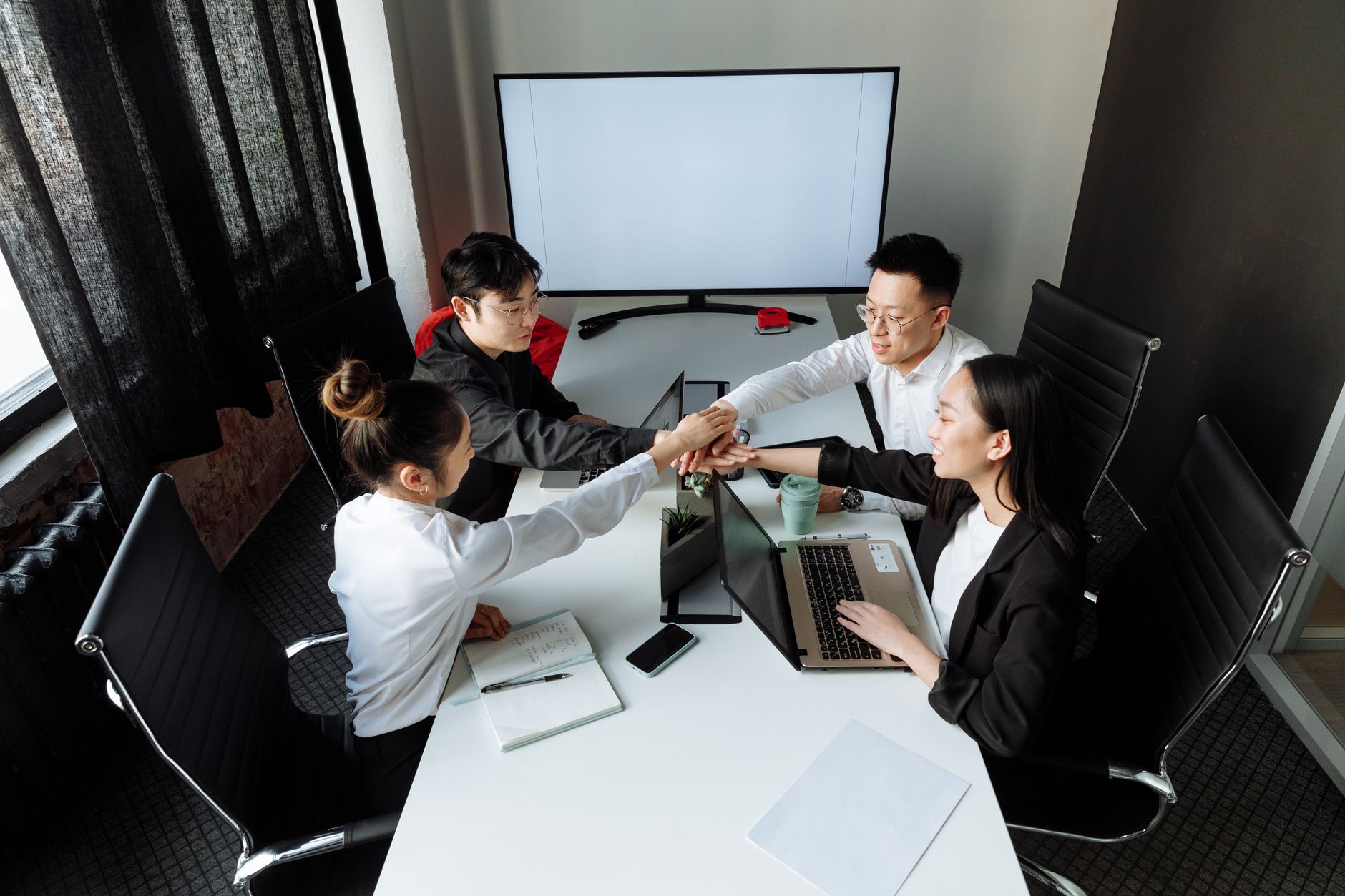 Quatre personnes réunissent leurs mains autour d’une table avec des ordinateurs portables.